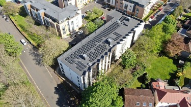 Aerial view of modern apartment building beside leafy residential streets.